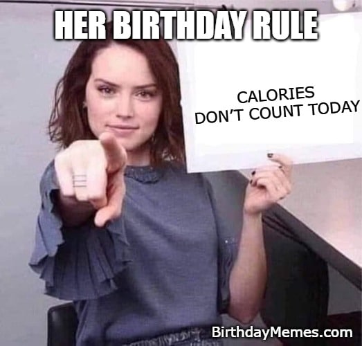 Woman pointing at a sign that says “Calories don’t count today” because it’s her birthday, proving she’s ready to eat cake without a single ounce of guilt.